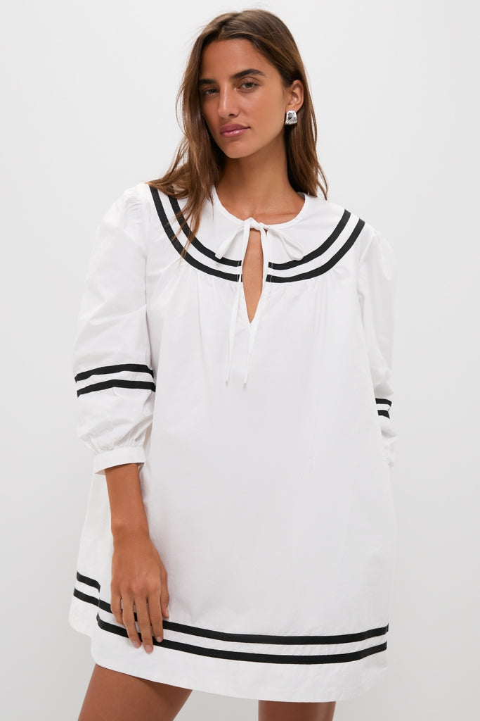 Model wearing the classic White Palina Mini Dress with bold black stripes, featuring a keyhole tie detail and three-quarter sleeves, exuding effortless, high-end vacation style.