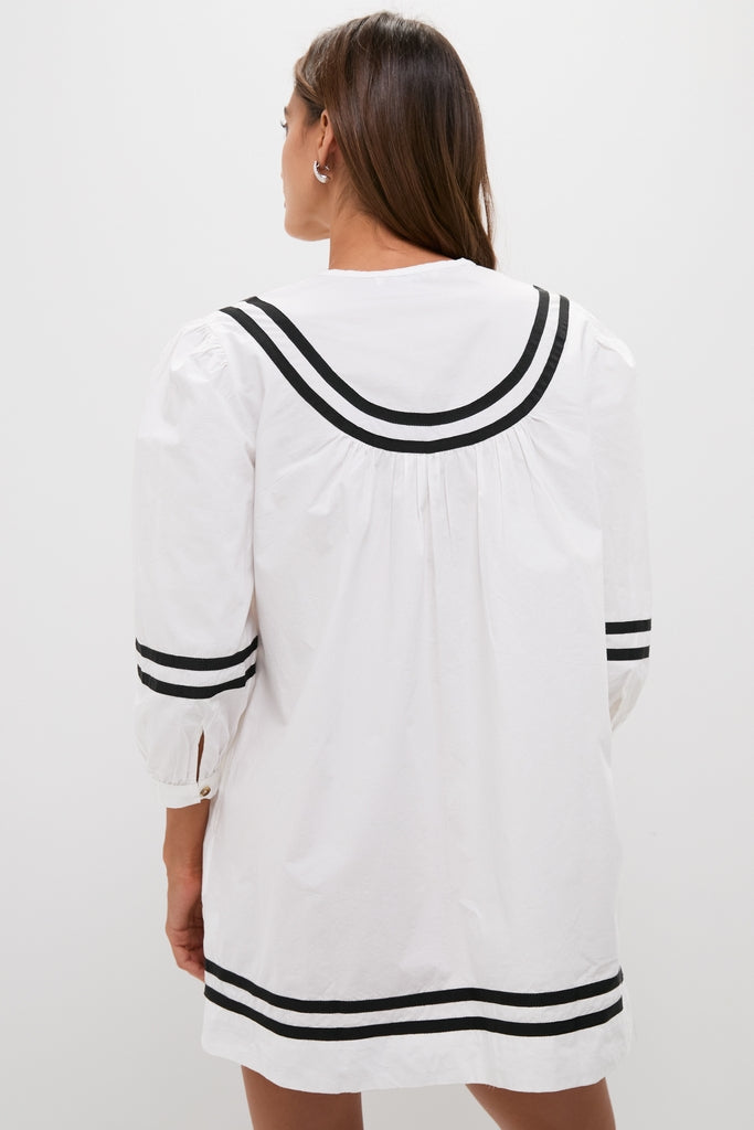 Back view of a woman in the classic White Palina Mini Dress with black striped trim, embodying effortless, high-end vacation style.