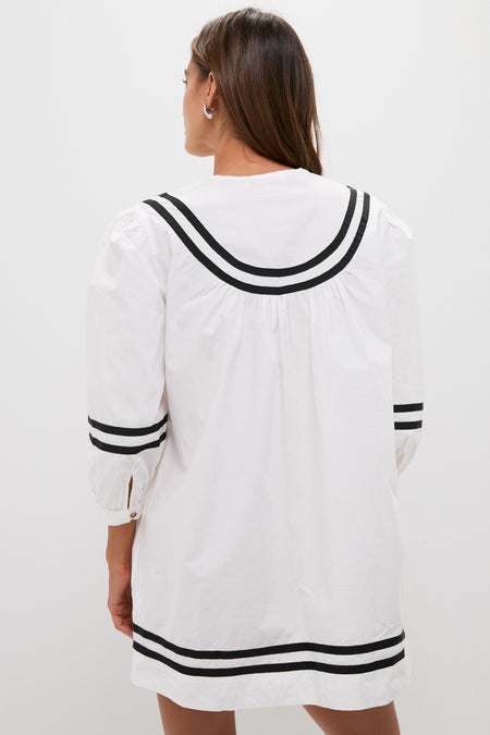 Back view of a woman in the classic White Palina Mini Dress with black striped trim, embodying effortless, high-end vacation style.