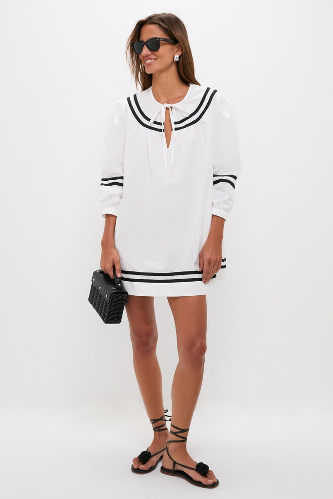 Woman in the classic White Palina Mini Dress with contrast trim, styled effortlessly with flat sandals and sunglasses, exuding a fun, high-end, vacation-ready vibe.