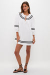 Woman in classic White Palina Mini Dress with black stripe details, modeling effortless style. Paired with black sandals and silver earrings, embodying high-end, fun vacation wear.