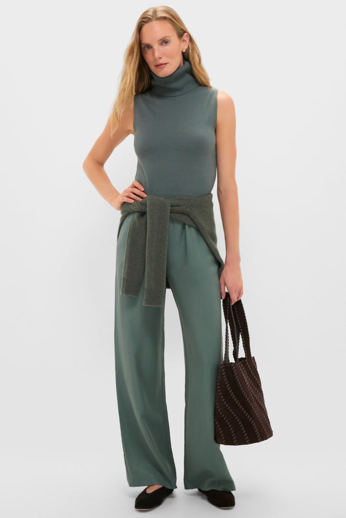 Model wearing the classic Eucalyptus Zoe Sleeveless Turtleneck, paired with matching trousers and a woven tote, embodying effortless, high-end style.