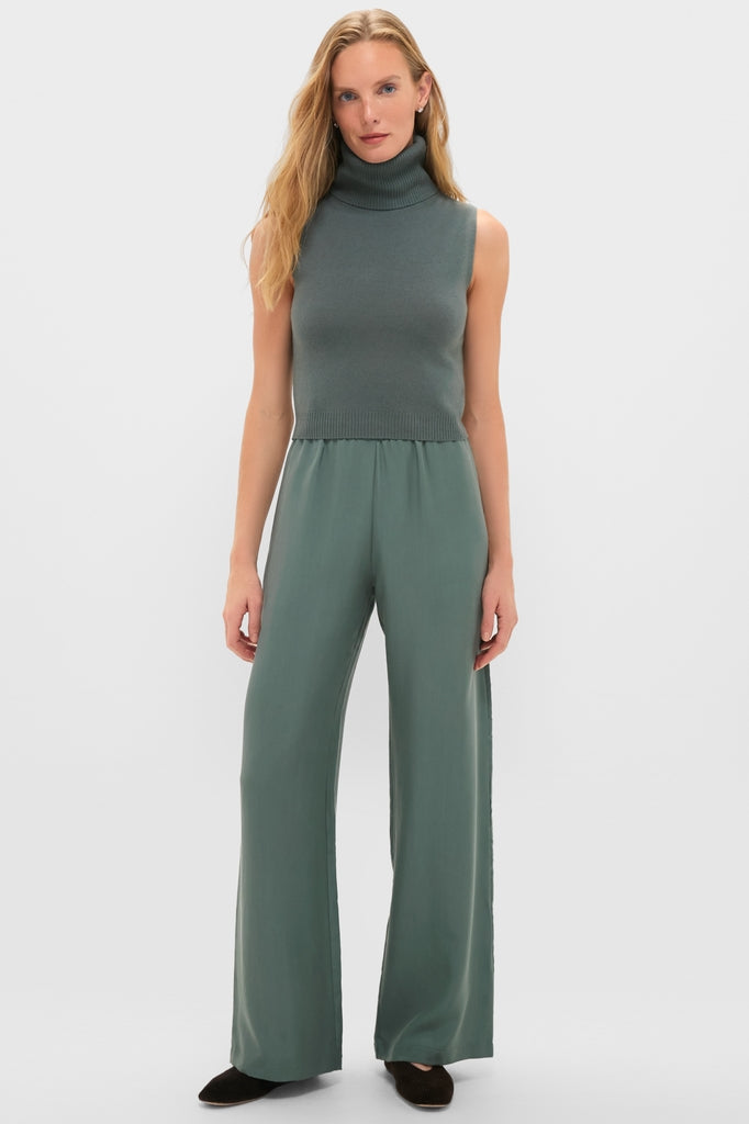 Woman models the Eucalyptus Zoe Sleeveless Turtleneck with high-waisted trousers, embodying an effortless, high-end style. The classic, minimalist ensemble is both fun and sophisticated.