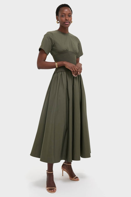Woman models the Fern Wrenna Short Sleeve Midi Dress, an effortless, classic olive-green gown with a smocked waist, styled with gold accessories and high-end sandals.