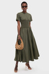 Woman models the Fern Wrenna Short Sleeve Midi Dress, an olive-green classic with a flared skirt, styled effortlessly with chic accessories for a fun, high-end look.