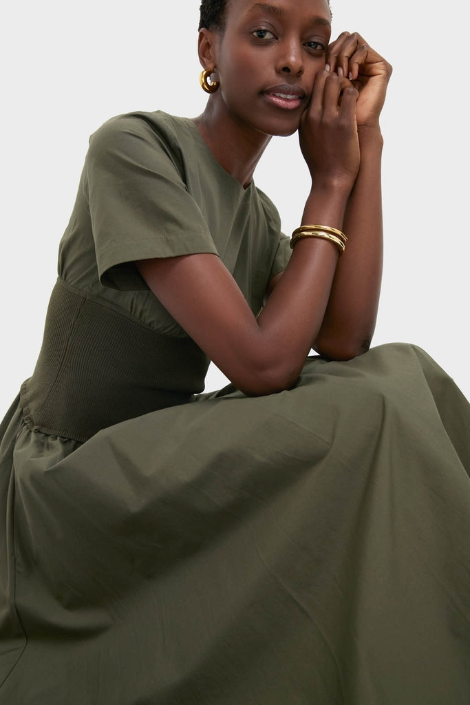 Woman in an olive-green Fern Wrenna Short Sleeve Midi Dress, showcasing a classic and effortless style with a fitted waistband, accessorized with gold hoop earrings and bangles.