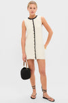 Model wearing the White Knit Lalia Mini Dress with black crochet trim, accessorized with a black bucket bag, gold jewelry, and black sandals, showcasing an effortless, classic style.