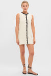 White Knit Lalia Mini Dress: A classic, effortless crochet mini with black scalloped trim and gold buttons, styled with flat sandals for a fun, high-end look.
