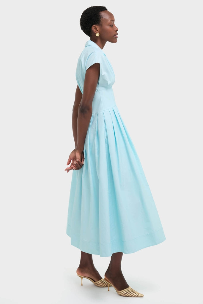 Woman in profile wearing the Sky Farlow Midi Dress, a classic, sleeveless, pleated design with a fitted bodice, paired effortlessly with high-end gold mule shoes.