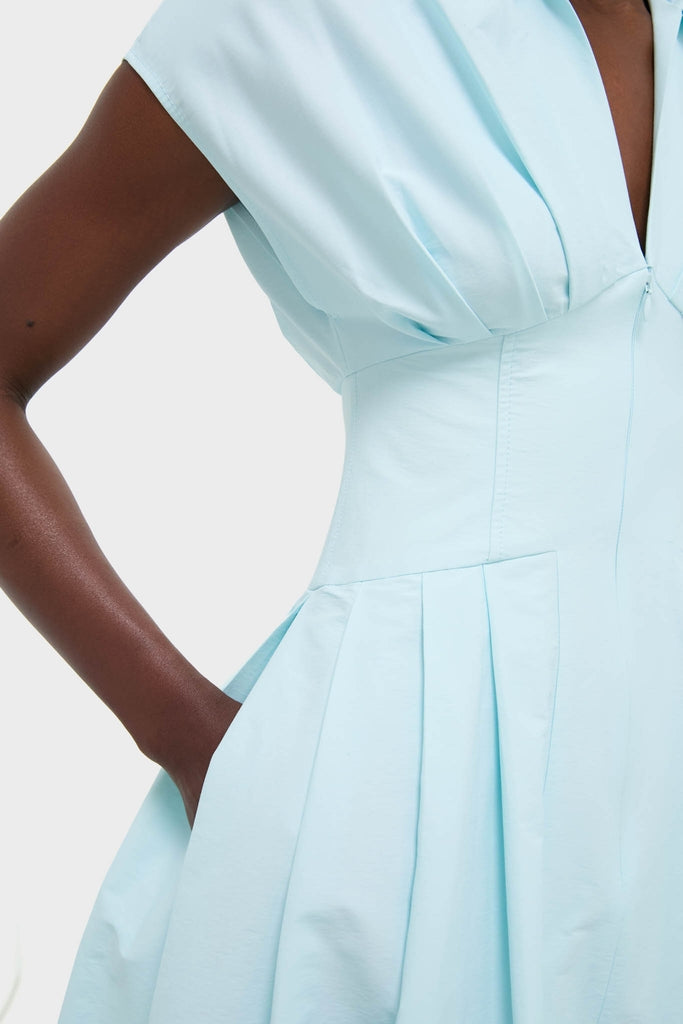 Person wearing the Sky Farlow Midi Dress—an effortless, classic pale blue sleeveless dress with a deep V-neck, fitted waist, and pleated skirt, embodying high-end, fun style.