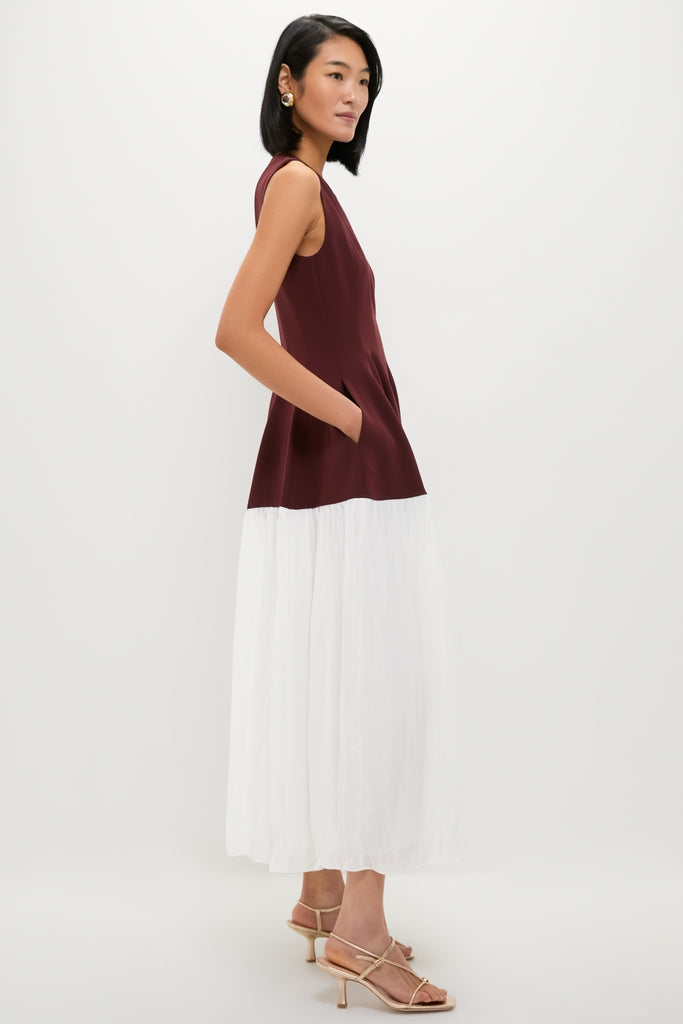 Model in sleeveless Mahogany Multi Raleigh Midi Dress with burgundy bodice and flowing white skirt, accessorized with gold hoop earrings, embodies classic, effortless style.