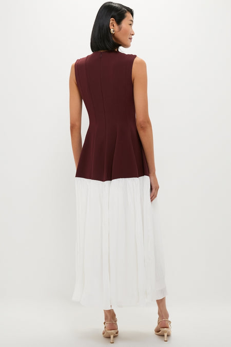 Woman models the Mahogany Multi Raleigh Midi Dress, featuring a classic burgundy peplum top and an effortless white midi skirt, paired with fun, high-end beige sandals.