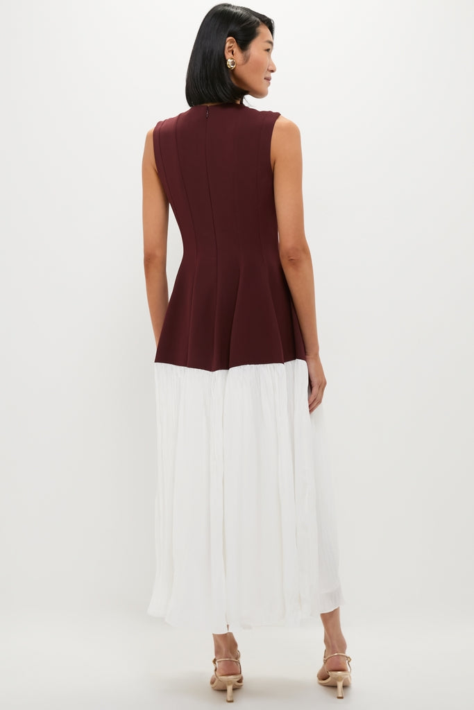 Woman models the Mahogany Multi Raleigh Midi Dress, featuring a classic burgundy peplum top and an effortless white midi skirt, paired with fun, high-end beige sandals.