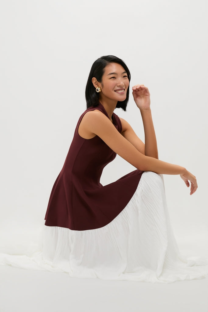 Model in profile wearing the classic Mahogany Multi Raleigh Midi Dress, featuring a sleeveless burgundy top and an effortless white pleated skirt, embodying a high-end, fun style.