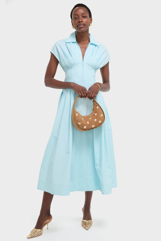 Woman in an aqua-blue dress holds the classic Camel Finn Studded Suede Shoulder Bag, effortlessly styled with gold accents for a fun, high-end look.