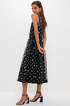 Woman models Black Embroidered Mariella Midi Dress with white floral motifs, gathered waist, and semi-sheer yoke, paired with strappy high-heels for a classic, effortless look.