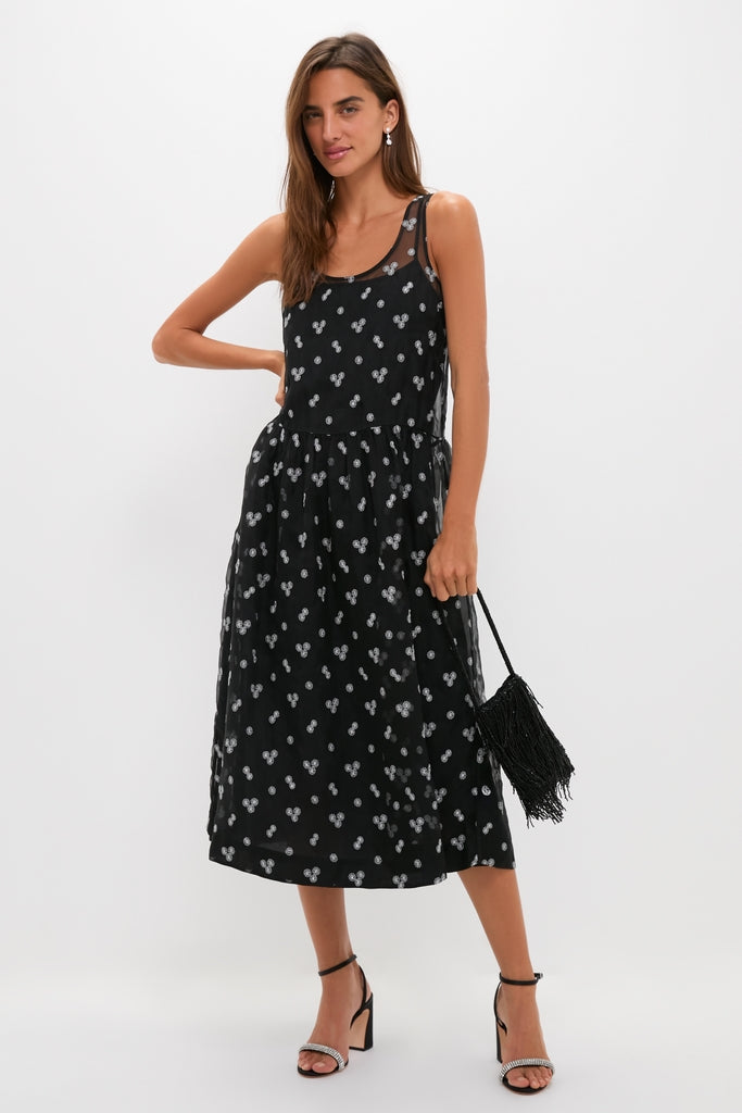 Woman in classic Black Embroidered Mariella Midi Dress with sheer yoke, silver motifs, accessorized with earrings, fringed handbag, and high-heeled sandals, embodying effortless, high-end style.