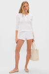 Young woman wearing a classic White Pointelle Long Sleeve Henley Tee with matching shorts, exuding an effortless, high-end style, complemented by ballet flats and a canvas tote.