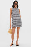 Model wearing the classic Black and White Gingham Mini Dress with pockets, paired effortlessly with black strappy sandals and sunglasses, holding a woven straw handbag for a fun, high-end look.