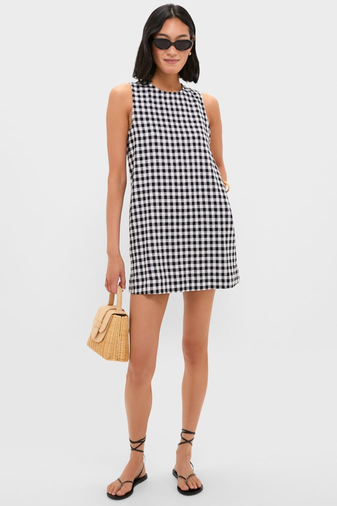 Model wearing the classic Black and White Gingham Mini Dress with pockets, paired effortlessly with black strappy sandals and sunglasses, holding a woven straw handbag for a fun, high-end look.