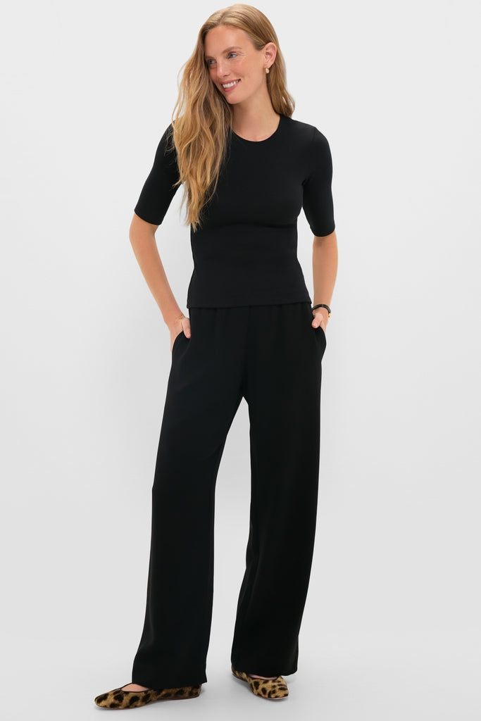 Woman models classic Black Arielle Pocket Pants with a relaxed silhouette and side pockets, styled effortlessly with a matching top and fun leopard-print shoes.