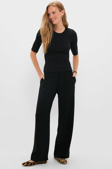 Woman models classic Black Arielle Pocket Pants with a relaxed silhouette and side pockets, styled effortlessly with a matching top and fun leopard-print shoes.