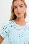 Young woman in a classic, light-blue Sky Emrys Mini Dress with laser-cut details, exuding an effortless, high-end style, accented by small gold hoop earrings.