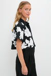 Young woman in a classic Black Multi Callie Camp Shirt with large white florals, exuding effortless, high-end style, paired with high-waisted trousers for a fun, confident look.