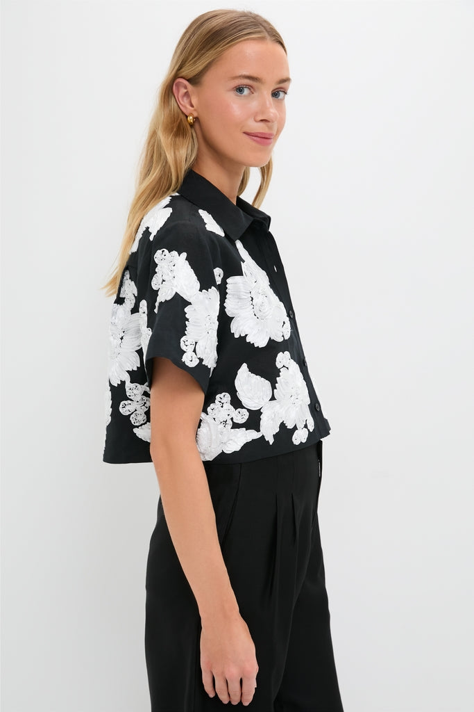 Young woman in a classic Black Multi Callie Camp Shirt with large white florals, exuding effortless, high-end style, paired with high-waisted trousers for a fun, confident look.