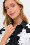 Young woman in the Black Multi Callie Camp Shirt with floral embroidery, embodying a classic and effortless style, touching the collar, showcasing high-end, fun fashion.