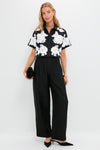 Woman models the classic Black Multi Callie Camp Shirt with floral appliqués, paired with black wide-leg pants and clutch, embodying an effortless, high-end style.