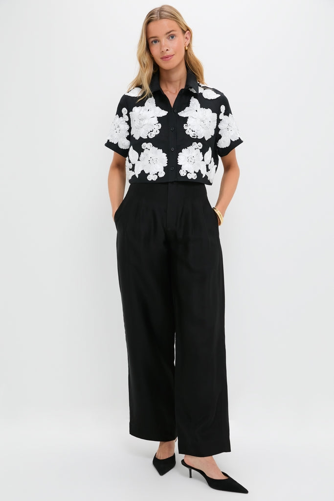 Woman wearing the Black Multi Callie Camp Shirt with large floral appliqués, paired with high-waisted, wide-leg trousers. A classic, effortless look with high-end appeal.