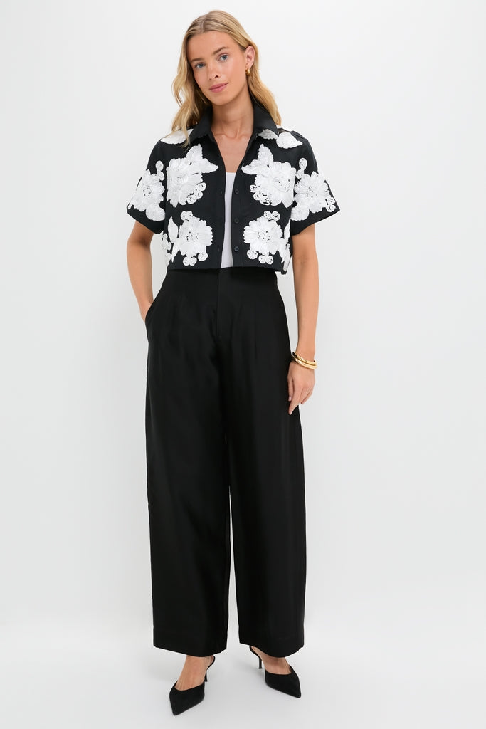 Model wearing the Black Multi Callie Camp Shirt with white floral appliqués, styled with high-waisted trousers and gold accessories. A classic, effortless high-end look.