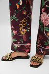 Black Faye Beaded Leather Flat Slides with a chunky gold-tone chain-link strap, embodying effortless elegance and classic style, paired with tropical-print pants for a fun, high-end look.