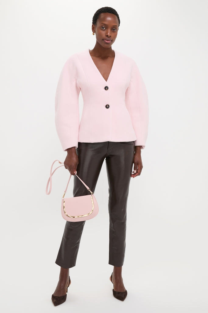 Model in sleek black leather pants, classic V-neck blazer, and pointed heels, showcasing the effortless and high-end Pale Pink Logan Leather Crossbody with gold hardware.