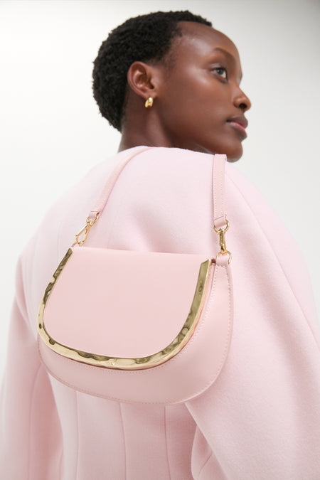 Woman wearing a Pale Pink Logan Leather Crossbody with a curved flap and hammered gold hardware, exuding a classic and effortless high-end style.