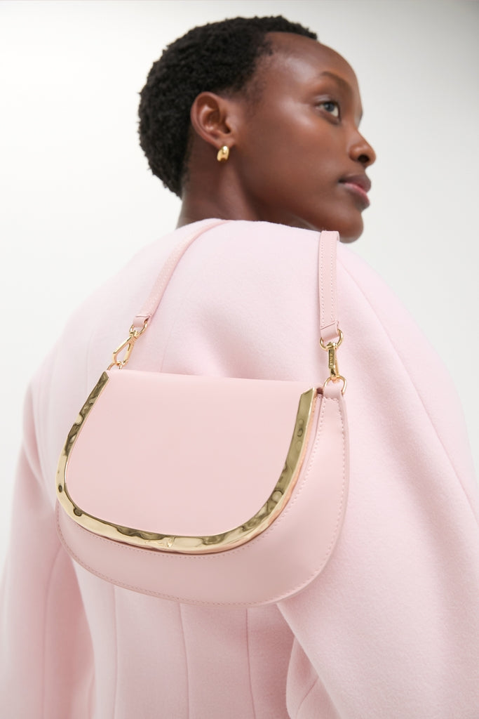 Woman wearing a Pale Pink Logan Leather Crossbody with a curved flap and hammered gold hardware, exuding a classic and effortless high-end style.