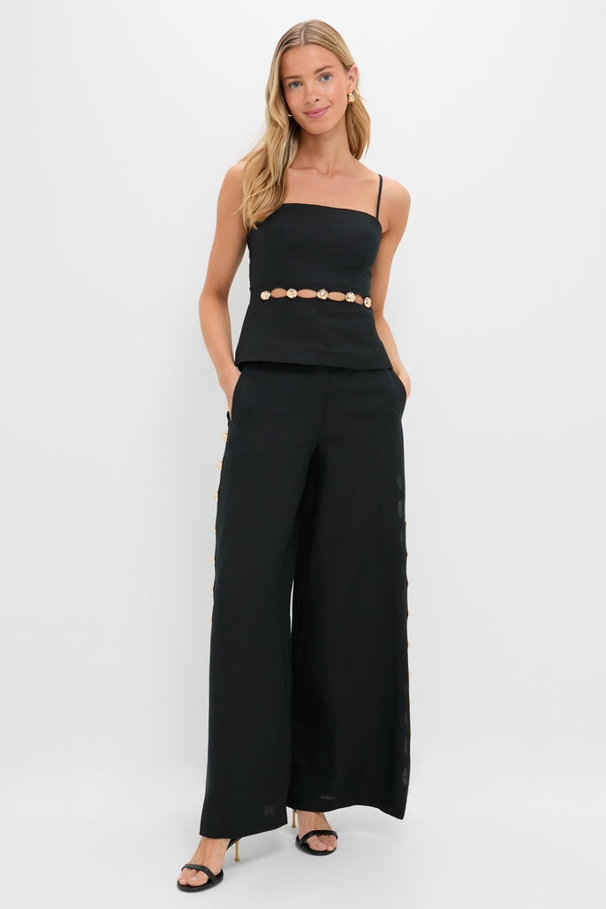 Model wearing the Black Cruz Cami with gold hardware and waist cutouts, paired with high-waisted, wide-leg trousers. Effortless, classic, and high-end ensemble with fun, polished details.