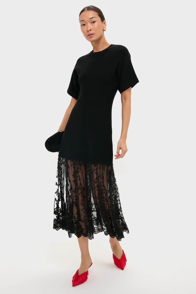 Model wearing classic black dress with sheer lace skirt, holding a black clutch, and showcasing effortlessly stylish Red Stain Inez Heels, embodying fun and high-end elegance.