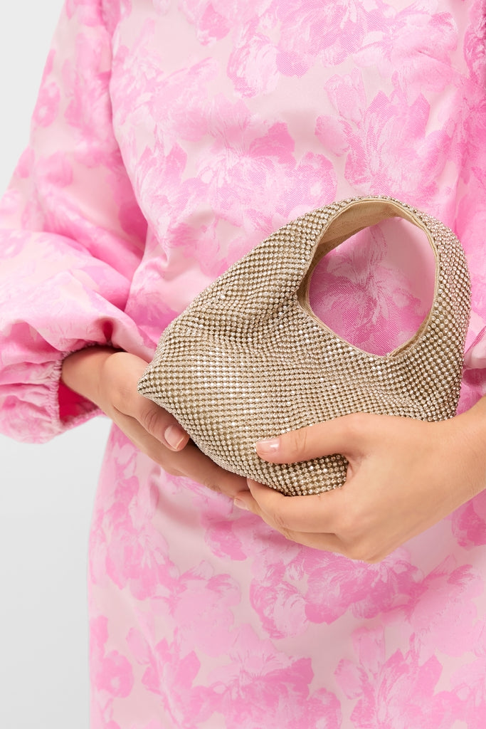 Gold Diamante Kenzie Bag: a classic, high-end evening clutch, fully adorned with sparkling rhinestones. Effortlessly chic, held by a person in a pink, floral blouse.