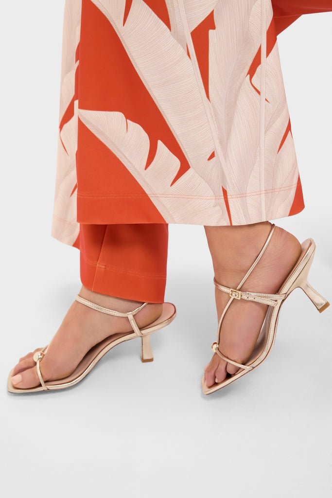 Close-up of model wearing Champagne Metallic Triana Heels: classic, effortless gold strappy sandals with a fun T-strap design and elegant kitten heel, embodying high-end style.