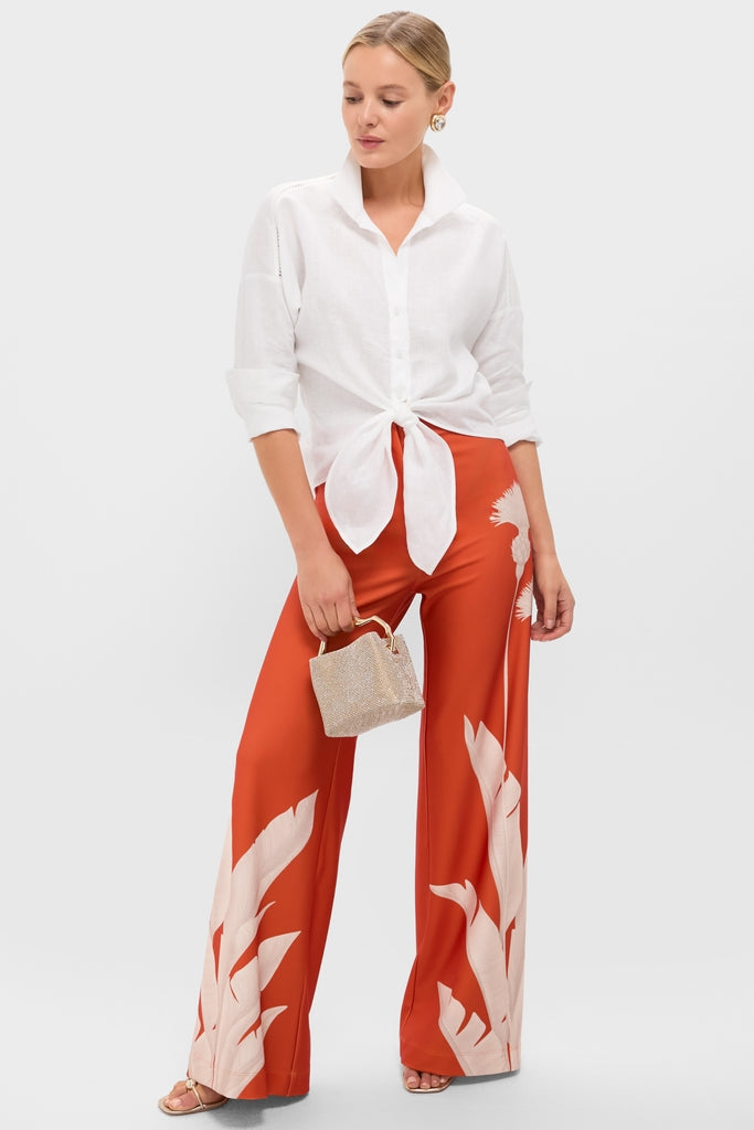 Model in classic white shirt, burnt-orange trousers, holding Champagne Metallic Triana Heels; effortless style with gold-tone sandals and statement earrings, embodying fun, high-end elegance.