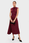 Woman models a classic deep burgundy dress, showcasing Gold Smooth Moves Earrings with fringe and floral details, embodying effortless, high-end elegance, holding a black clutch.