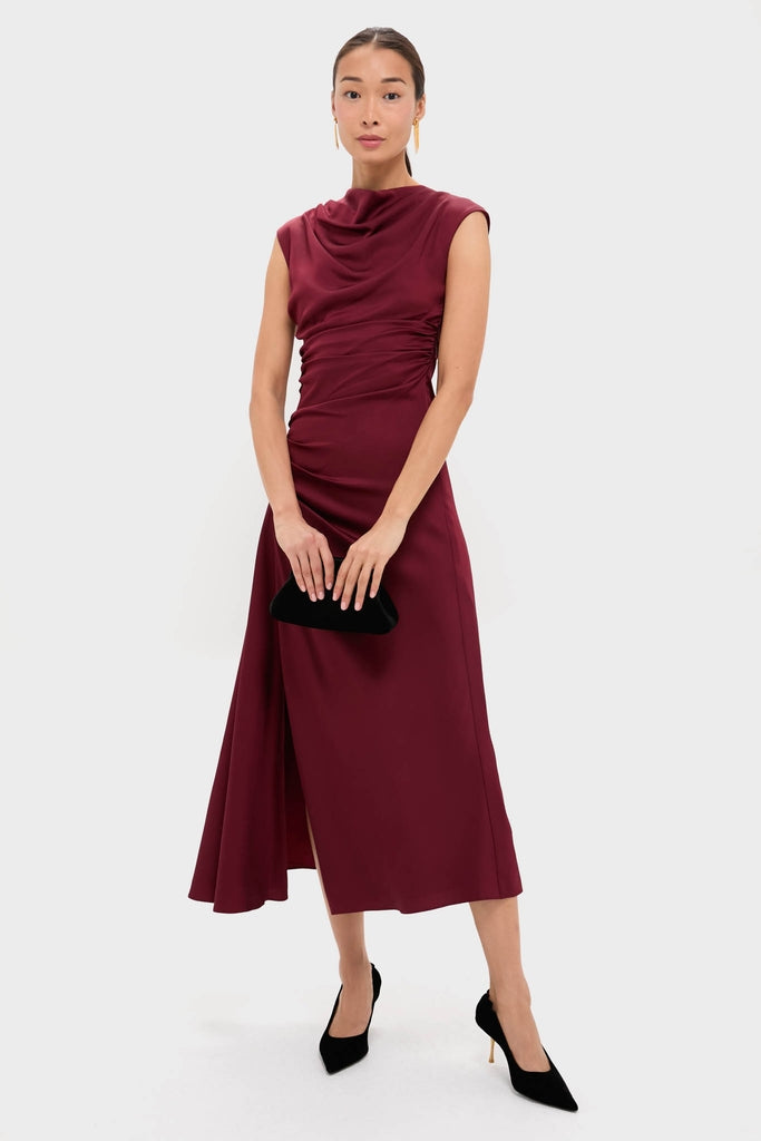 Woman models a classic deep burgundy dress, showcasing Gold Smooth Moves Earrings with fringe and floral details, embodying effortless, high-end elegance, holding a black clutch.