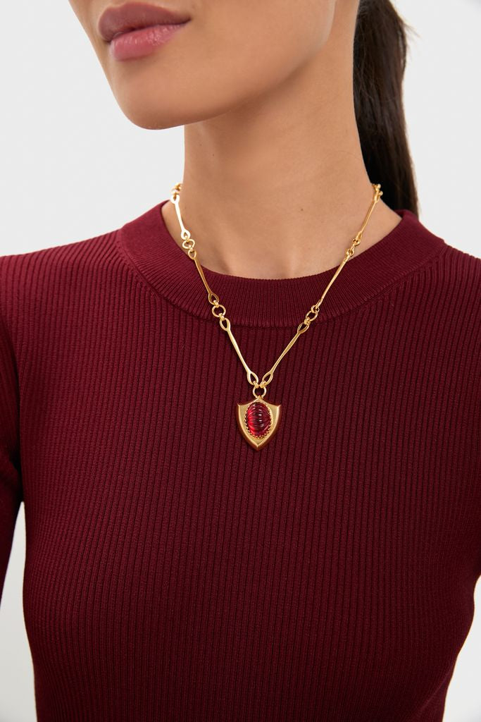 Woman wearing the Red Lettie Necklace, a classic gold-tone chain with a shield-shaped pendant featuring a glossy red stone, exuding effortless and high-end style.