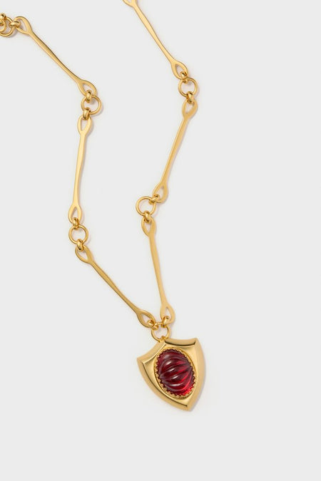 Red Lettie Necklace: A classic gold-tone chain with elongated links, featuring an effortless, high-end shield pendant with a deep red cabochon gemstone, perfect for fun occasions.