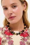 Young woman wears the Brown Tommie Necklace, a classic set of glossy black beads with gold-tone accents, paired with chunky gold hoops, exuding effortless high-end style.
