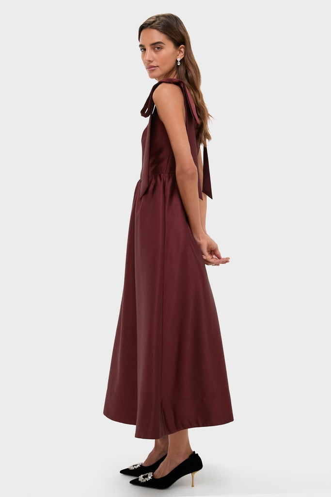Woman in Oxblood Dupioni Bow Esme Dress, showcasing a classic, effortless silhouette with bow-tied straps and a fit-and-flare skirt, paired with black pumps.