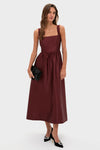 Model in classic Oxblood Dupioni Bow Esme Dress, featuring a square neck and gathered waist, styled with black clutch and heels for an effortless, high-end look.