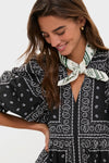 Woman in black paisley-print dress wears the HB x Tuckernuck Stars at Night Scarf, a classic, effortless accessory with green star motifs. She exudes a fun, high-end vibe.